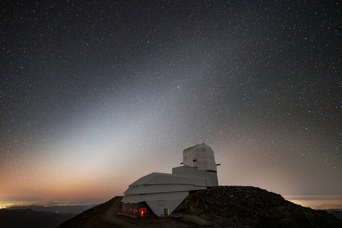Vera C. Rubin Observatory sits under the faint glow of a fascinating astronomical phenomenon known as zodiacal light. It appears as a faint, cone-shaped glow that extends along the path followed by the planets and Sun (known as the ecliptic) and is caused by sunlight reflecting off interplanetary dust that sits in the plane of our Solar System. This phenomenon is most easily seen in the western sky just after sunset or in the eastern sky just before sunrise. The dust is thought to be left by comet tails and collisions between asteroids. Zodiacal light is faint and usually drowned out by light-polluted skies or glare from the Moon.  The NSF–DOE Vera C. Rubin Observatory is funded by the U.S. National Science Foundation (NSF) and the U.S. Department of Energy’s Office of Science (DOE/SC). Rubin Observatory is a Program of NSF NOIRLab, which, along with DOE’s SLAC National Accelerator Laboratory, will jointly operate Rubin. Rubin Observatory is being built on Cerro Pachón, Chile which is one of the best observing sites in the southern hemisphere, making it a great place to capture such a rare sight as zodiacal light. When complete it will use its 8.4-meter mirror combined with the largest camera ever built for astronomy to begin an ambitious decade-long survey of the southern sky called the Legacy Survey of Space and Time (LSST) that will help answer some of the biggest questions about the Universe. Rubin Observatory will begin science operations in late 2025. This photo was taken by Hernán Stockebrand, NOIRLab Audiovisual Ambassador.